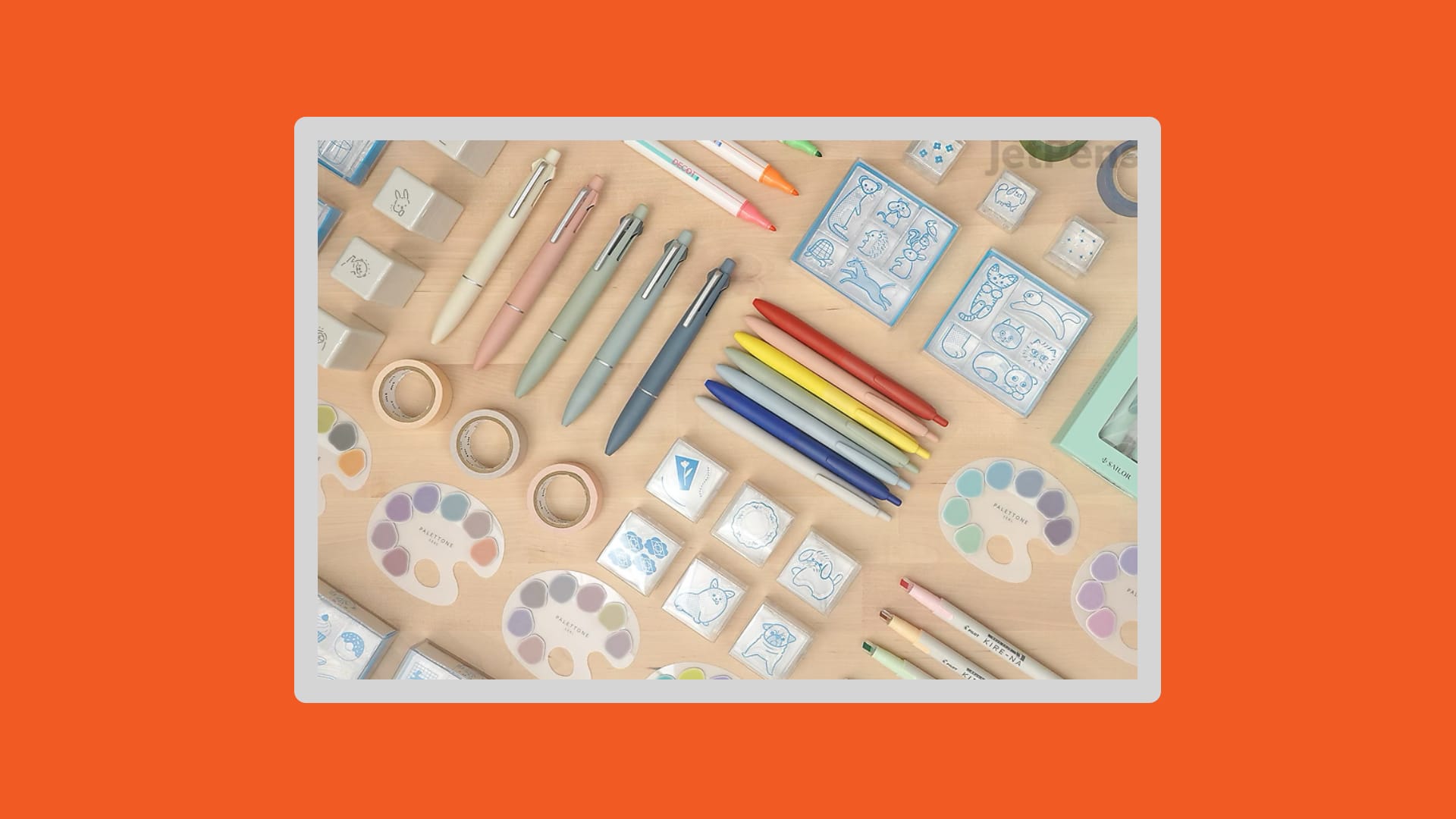 Top-down shot of different pens, highlighters, and stickers that won stationary awards on an orange background.