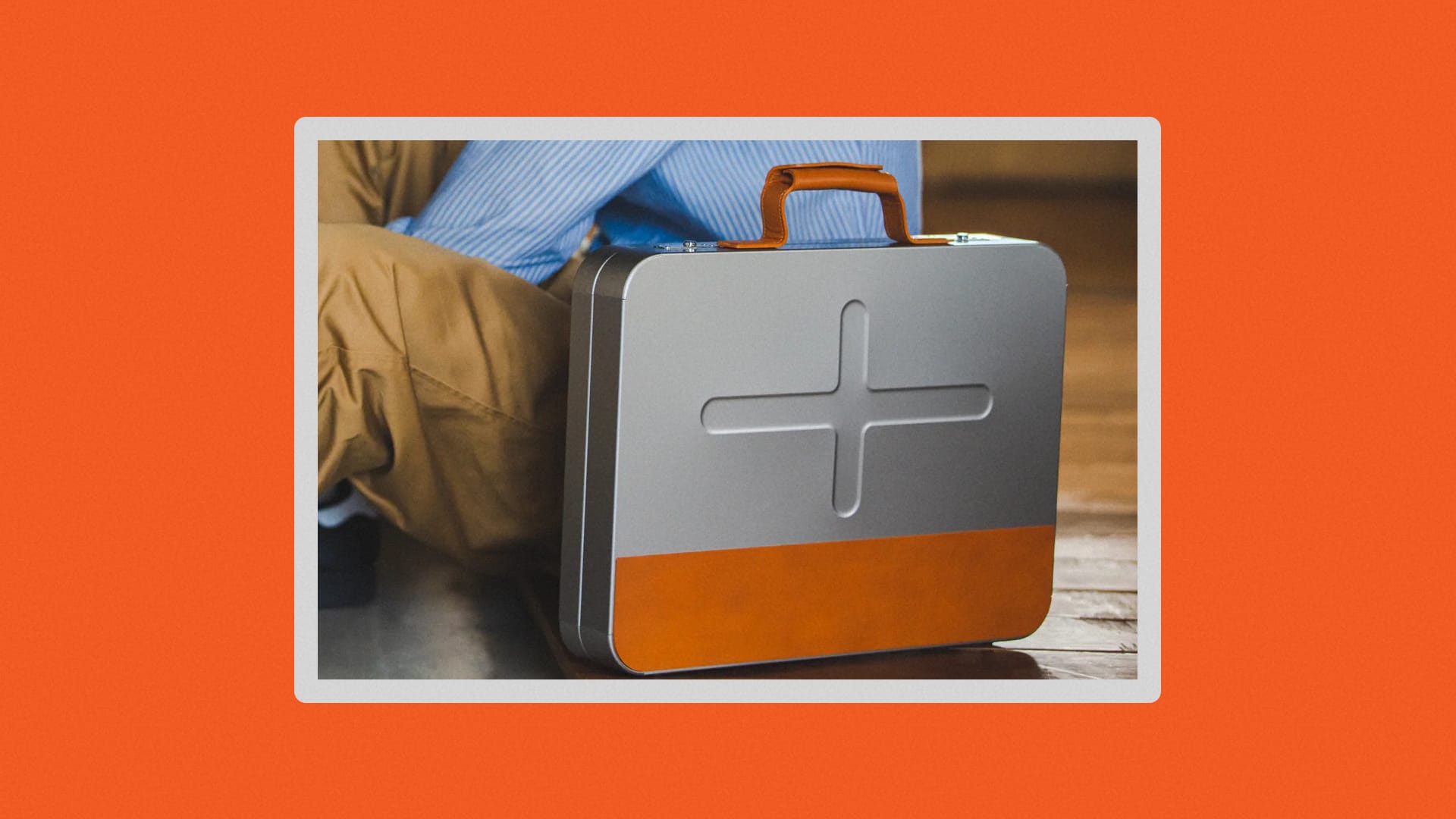 Aluminum and leather briefcase next to a man sitting on the floor.